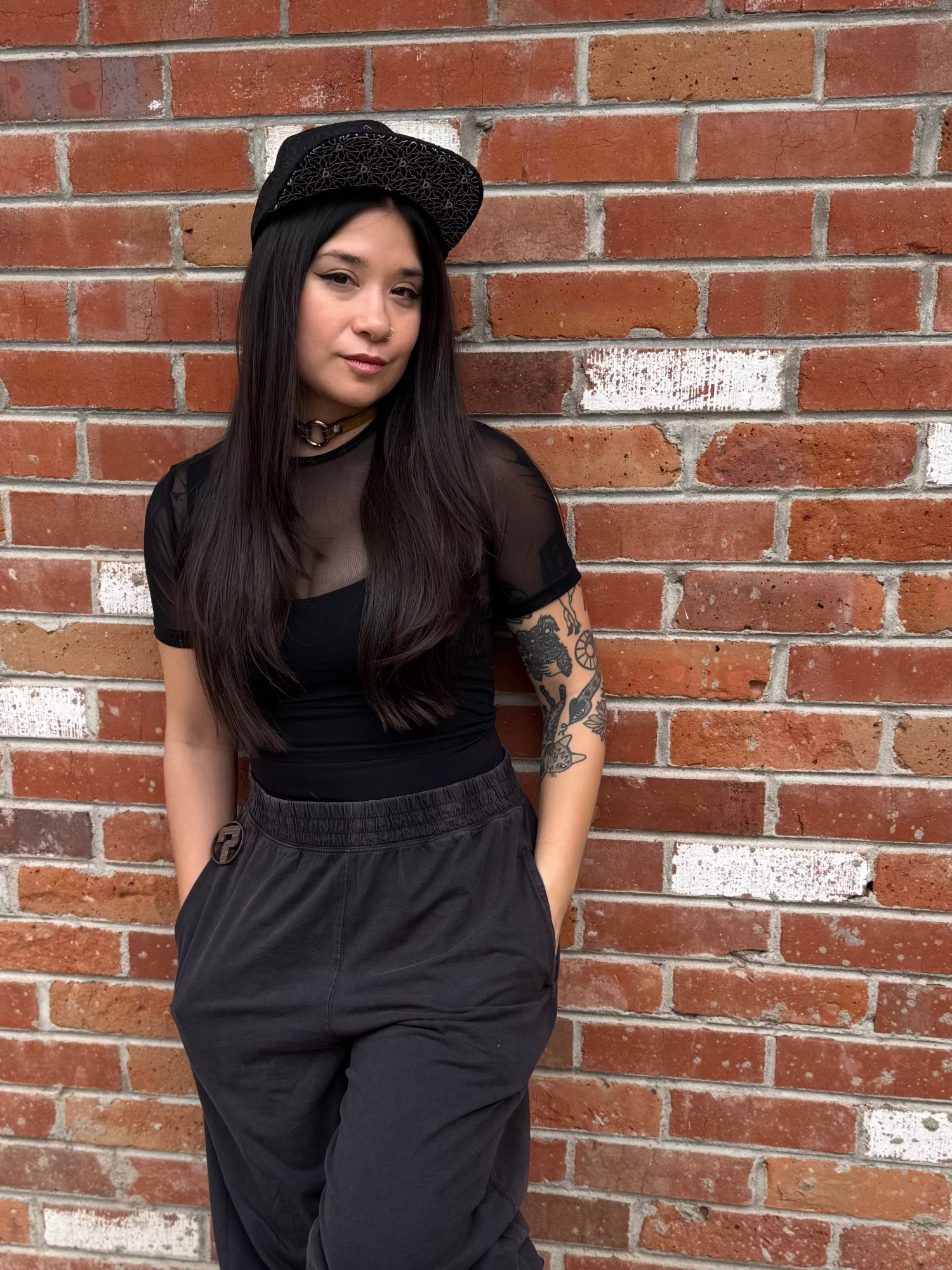 Person wearing a black outfit with sheer top against a brick wall, product image for a hat that was designed by nectar collective and snapback grassroots